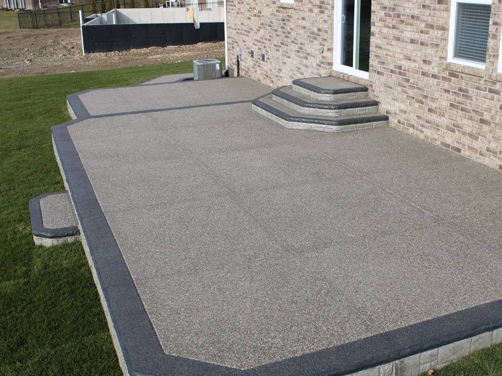 Exposed aggregate patio and steps sealed in a matte finish beside a brick home