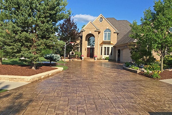 Stamped concrete driveway after gloss sealing in front of a brick home